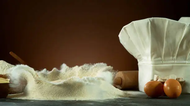 Freeze motion of falling yeast dough into flour. Ingredients for cooking, preparation concept with cooking cap.