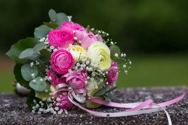 Colorful bridal bouquet with red and yellow flowers and white and pink ribbons that sits on a dark stone wall