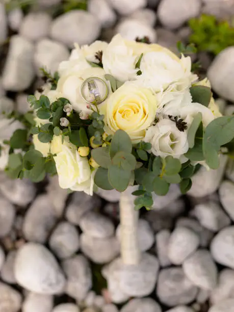 Bright bridal bouquet with roses lying on the floor with large white gray pebbles. The rings of the bridal couple lie on top of each other on a rose blossom