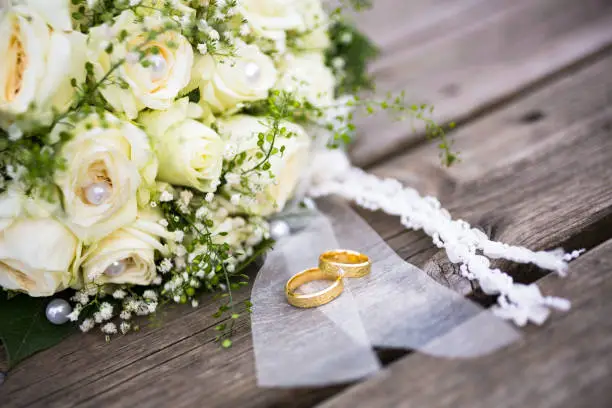 Bright yellow bridal bouquet with roses on a wooden board floor and the golden rings in the foreground