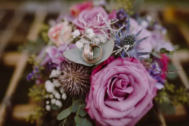 Colorful bridal bouquet lying on a wooden surface. The rings of the bridal couple lie on top of each other on a green leaf of the bouquet