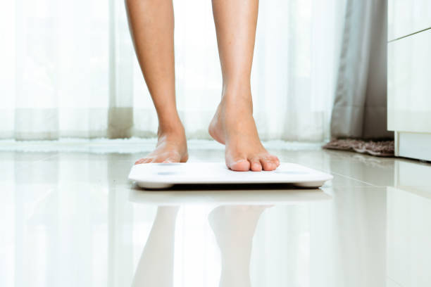 istock Female leg is stepping on white scales at home 1247866928