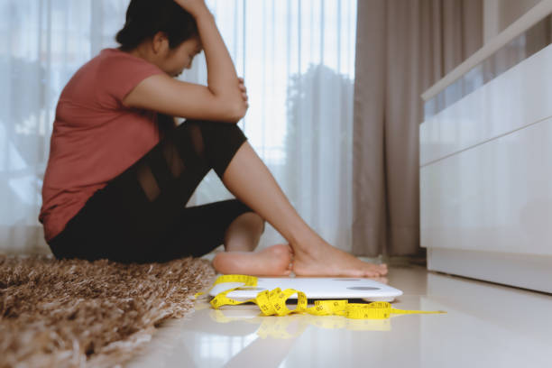 Weight loss fail concept. Scale and measure tape with depressed, frustrated and sad woman sitting on floor Weight loss fail concept. Scale and measure tape with depressed, frustrated and sad woman sitting on floor eating disorder stock pictures, royalty-free photos & images