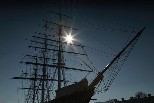 London, United Kingdom - Feb 23, 2019: The winter sun creates a sun star effect in the masts of the Cutty Sark. The Cutty Sark is a silhouette. The clipper carried tea from China, but was made obsolete by steam ships and the Suez Canal. It is now at Royal museums, in Greenwich, London.