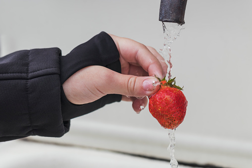 Soiled children's hands hold a red strawberry under water from an old tap. Grandma's vacation in the village. Healthy nutrition and natural vitamins.