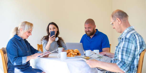 bonne famille multigénérationnelle lecture nouvelles le matin tout en mettant le petit déjeuner, se concentrer sur les jeunes - la démence numérique et la surutilisation du concept de technologie numérique - women telephone senior adult on the phone photos et images de collection