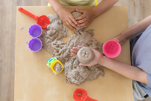 children's hands playing with kinetic sand and toys on the table. creative games concept. top view.