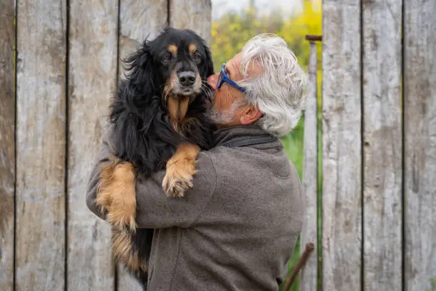 Man, in his 60s cuddling his dog outside. Photo is taken outdoors in spring.