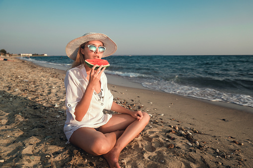 Young woman enjoying a slice of watermelon on the beach