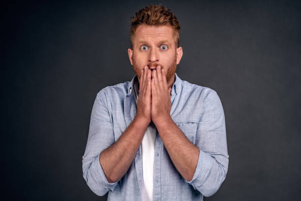istock Puzzled Caucasian redhead man covers mouth with both hands, has scared puzzled expression, cant believe in failure, stares through eyewear with bugged eyes, dressed in elegant shirt, stands indoor. 1247886671