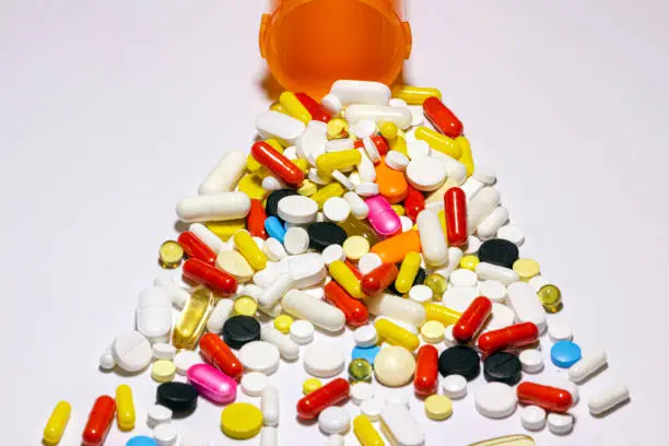 pills of various shapes, sizes and colors, scattered from an orange bottle on a light background.