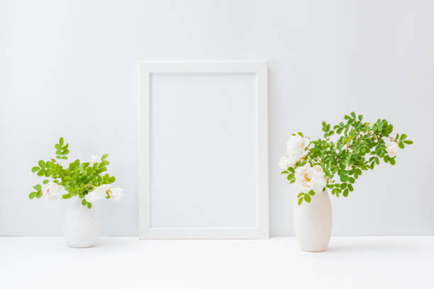 istock Home interior with decor elements. Mockup with a white frame and small flowers and green leaves in a vase on a light background 1247891742