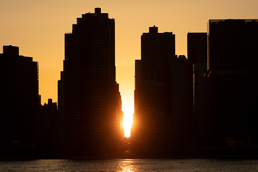 Sun setting behind the silhouette buildings of midtown Manhattan in New York City.