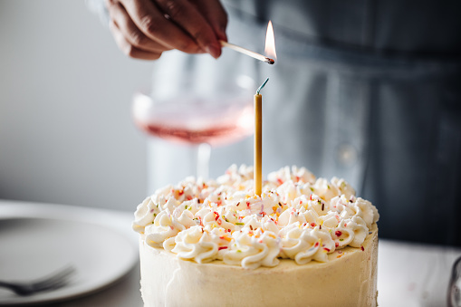 Close-up of a woman hand igniting birthday candle with a match stick. Cropped shot of a female burning a birthday candle over a cake.