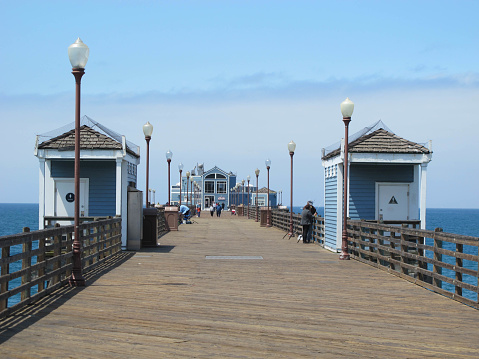 Oceanside, United States - May 16, 2013: The historic Oceanside Pier stretches into the Pacific Ocean, in Oceanside, California.  It is a wooden pier, measuring 1,942 feet in its 6th incarnation.  A pier has stood in Oceanside since the 1880s.  Tourists and locals alike head to the pier to fish, watch wildlife and hang out.