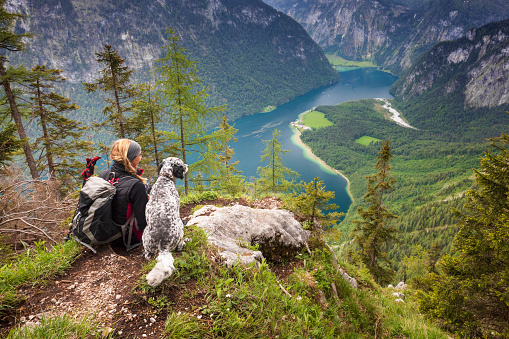 Germany, Bavaria, Berchtesgaden. \nA young woman sits on a view point with heer dog near Lake Königssee.