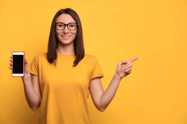 istock Pretty race mixed woman smiling, holding smartphone in her hand and pointing at blank space 1247921495