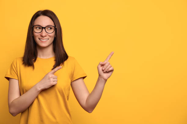 istock Pretty smiling girl pointing at copy space on yellow background 1247921709