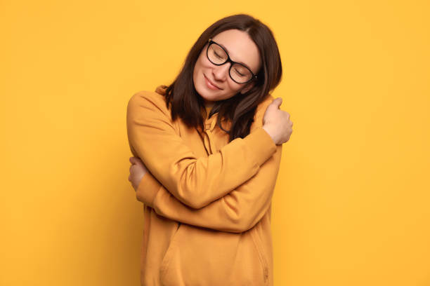 Beautiful happy girl with good self esteem hugging herself on yellow background