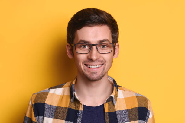 istock Attractive smiling guy in glasses posing against yellow studio wall 1247921751