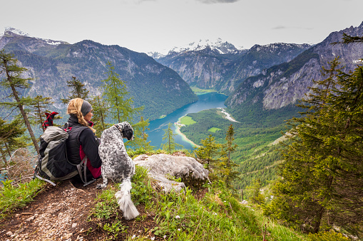 Germany, Bavaria, Berchtesgaden. \nA young woman sits on a view point with heer dog near Lake Königssee.