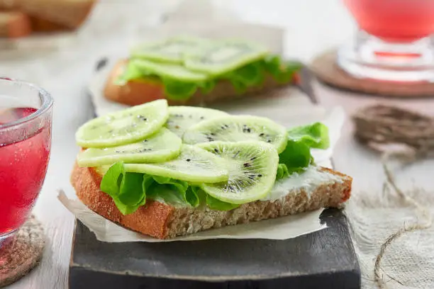 Photo of Sandwiches with soft cheese, salad and kiwi on the wooden cutting board. Romantic diet Breakfast for two.