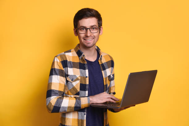 istock Young smiling guy posing with laptop against yellow studio wall 1247926155