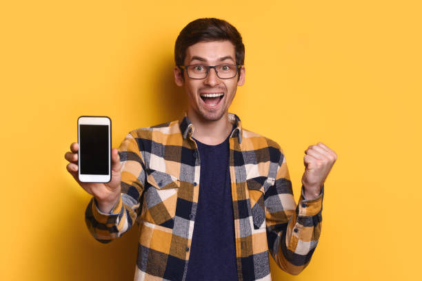 istock Happy guy holding cellphone and making yes gesture on yellow studio wall 1247926173