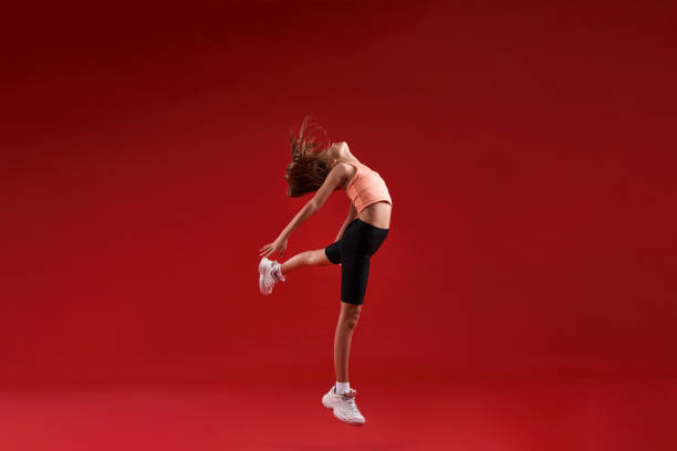 istock Practice with a purpose. A cute kid, girl is engaged in sport, she is looking up while jumping. Isolated on red background. Fitness, training, active lifestyle concept. Horizontal shot 1247928053