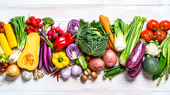 Healthy food: large group of  multicolored fresh organic vegetables arranged in a row shot from above on white table. Vegetables included in the composition are kale, tomatoes, squash, asparagus, potato, celery, eggplant, carrots, lettuce, edible mushrooms, bell peppers, cauliflower, ginger, radish, avocado, onion, chili pepper, corn, among others. High resolution 42Mp studio digital capture taken with SONY A7rII and Zeiss Batis 40mm F2.0 CF lens