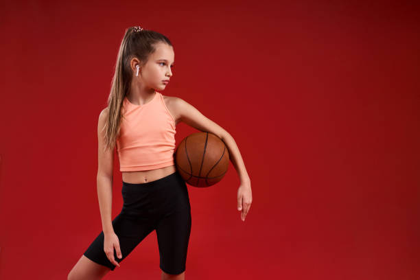 istock Ready for a game. A cute kid, girl is engaged in sport, she is looking aside while exercising with basketball. Isolated on red background. Fitness, training, active lifestyle concept. Horizontal shot 1247930109