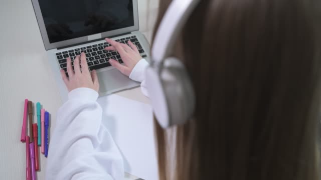 Girl in headphones types text on a laptop. Classes online without a face.