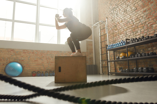 Sportive woman using plyo box while having workout at industrial gym. Horizontal shot. Selective focus