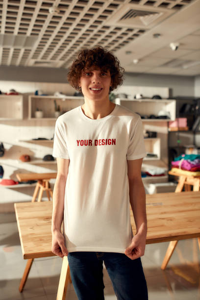 istock Design solutions. Young man smiling at camera, while trying on printed t shirt, standing in the store. Clothes at custom T-shirt, clothing printing company 1247962774