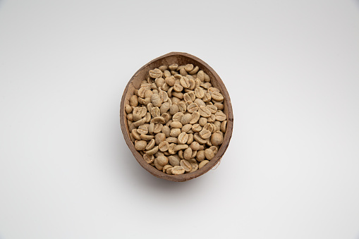 Close up shot of raw coffee beans in a coconut shell bowl isolated on white background with copy space