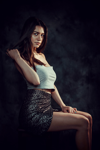 Portrait of beautiful long-haired brunette woman on black background. Female sit at table covered by black velvet. There are glass stones on the table and in hand.