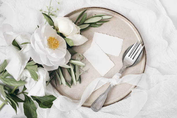 istock Festive summer wedding scene. Marble table setting with cutlery, olive branches, white peony flowers, stoneware plate and silk ribbon. Blank place cards mockups. Restaurant menu concept. Flat lay, top 1247969827