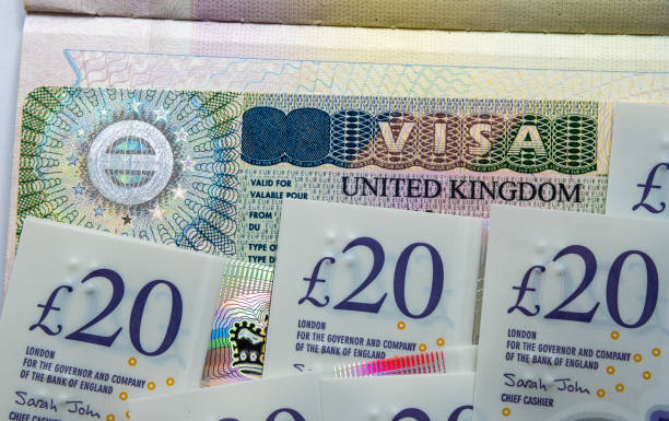 UK entry business and tourist visa in passport and pile of 20 pound banknotes. stock photo
