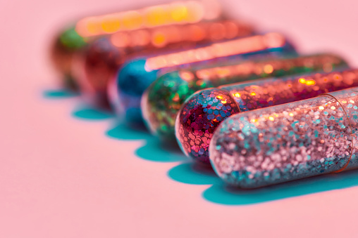 Creative concept with colorful glitter pills lying in a row isolated on pastel pink background. Minimal style, art concept. Horizontal shot. Web Banner