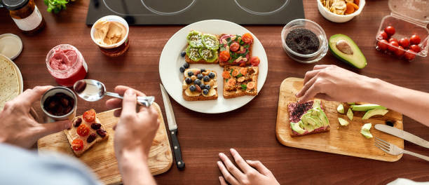 Top view of couple of vegetarians preparing various healthy toasts in the kitchen together. Man getting out sun dried tomatoes while woman adding chia seeds Top view of couple of vegetarians preparing various healthy toasts in the kitchen together. Man getting out sun dried tomatoes while woman adding chia seeds. Web Banner Avocado Toast with a Sprinkle of Chia Seeds stock pictures, royalty-free photos & images