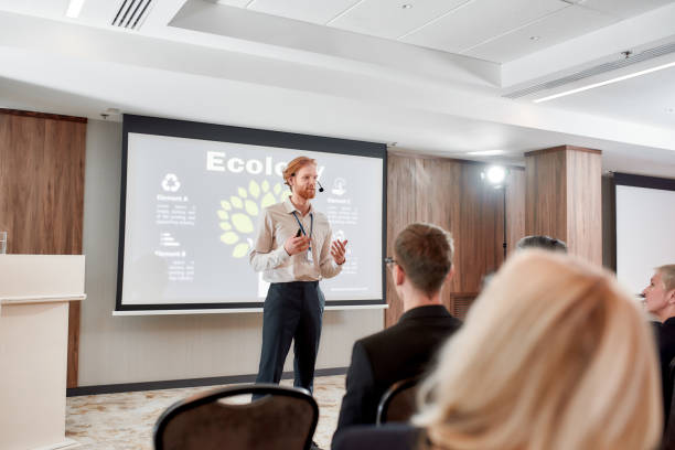 istock Teaching. Young male speaker in suit with headset and laser pointer giving a talk at business meeting, ecological forum 1247978202