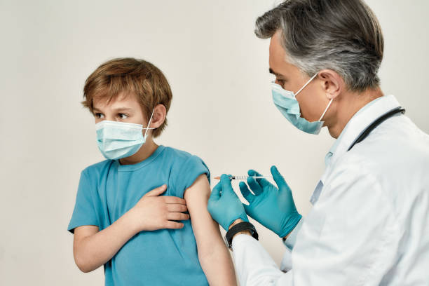 erhalt des impfstoffs. professioneller reifer arzt in medizinischer maske und blauen sterilen handschuhen, die injektion an einen kleinen jungen. immunisierung, medizin und gesundheitswesen - cute little boys caucasian child stock-fotos und bilder