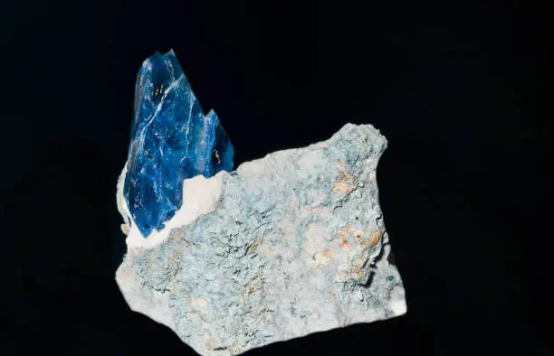 Benitoite is a rare blue barium titanium silicate mineral, found in hydrothermally altered serpentinite. Benitoite fluoresces under short wave ultraviolet light, appearing bright blue to bluish white in color. The more rarely seen clear to white benitoite crystals fluoresce red under long-wave UV light. Benitoite occurs in a number of sites, but gemstone quality material has only been found in California. It is California's official state gem.