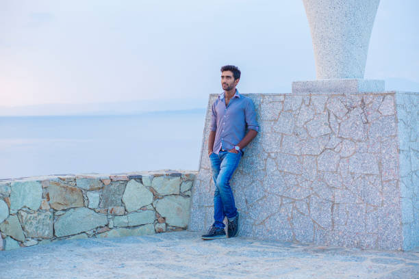 Man smiling looking up to blue sky taking deep breath celebrating freedom while standing near a concrete wall bridge above the sea. Positive person, peace mind concept. Free happy guy enjoying sunset