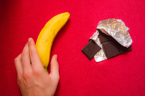 Over head shot of a hand selecting a banana to eat over a block of chocolate. Healthy living concept.