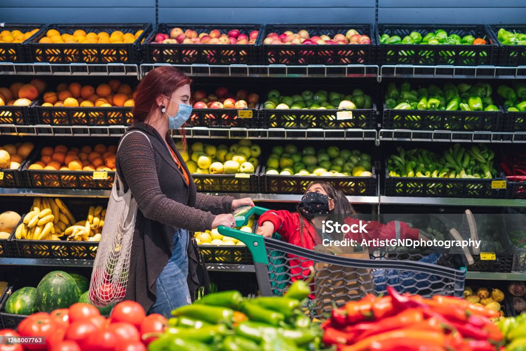 Asian Woman With Her Daughter Shopping In Supermarket With Face Protective Mask. Asian woman and her little daughter shopping fresh fruits and vegetables in supermarket with protective face mask. Supermarket Stock Photo