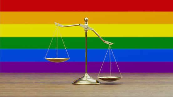 Bronze scale standing in front of LGBTI flag. Horizontal composition with copy space. Front view. Social justice concept.
