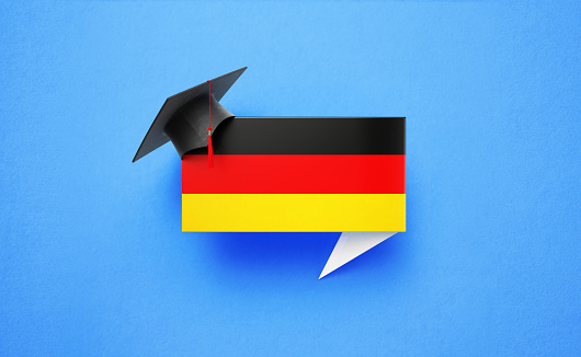 Graduation cap sitting over a speech bubble textured with German flag on blue background. Horizontal composition with copy space. Front view. Study in Germany concept.