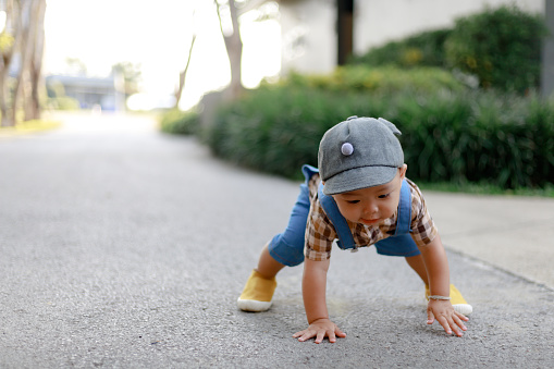 1 year old cute toddler Asia boy kid in bib jeans trying to stand up after fell with copy space.