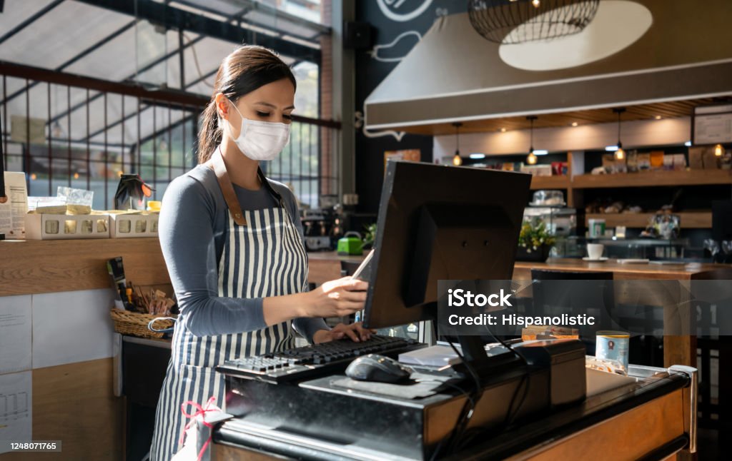 Waitress working at a restaurant wearing a facemask and placing the order in the computer Portrait of a waitress working at a restaurant wearing a facemask and placing the order in the computer - pandemic lifestyle concepts Restaurant Stock Photo